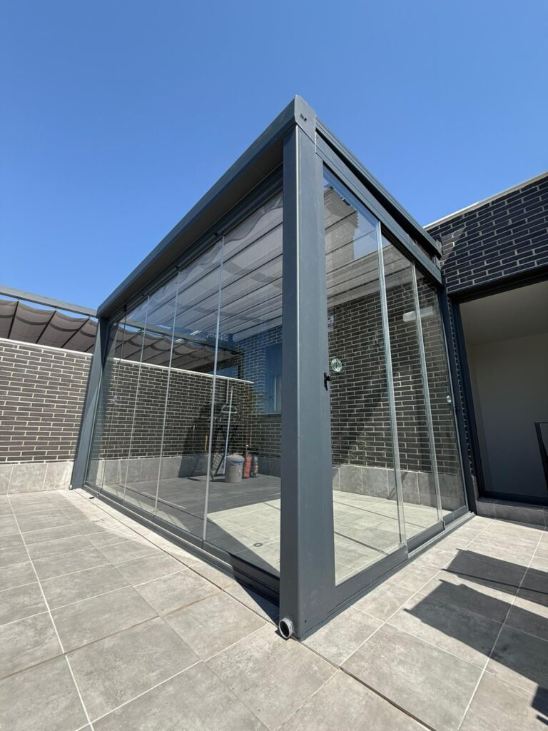 Pergola con control del clima mediante toldo palillero, cortina de cristal puerta corredera de tres hojas