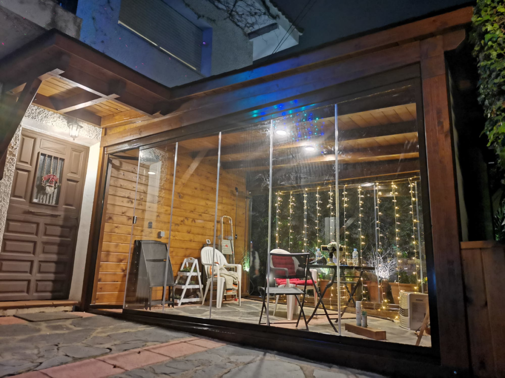 En la imagen se ve un porche rustico con una pared forrada de madera integrado en la entrada de la casa