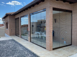 En la imagen se ve un porche de ladrillo con una cortina de cristal montada por la empresa
