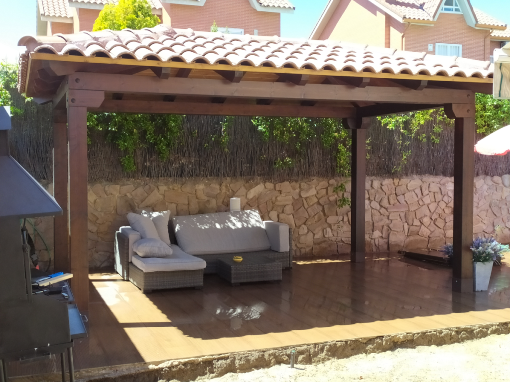 En la imagen se ve un porche a cuatro aguas al lado de una barbacoa en el jardin