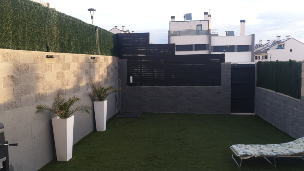 En la imagen se ve el jardin con la valla de madera sobre muro de bloques al fondo